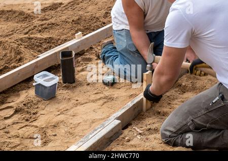 Concrete Worker using hammer to stake as they add wood framework for new sidewalk at new residential home construction site. Shallow depth of field fo Stock Photo