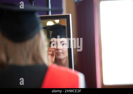 A female European Graduate gets ready for the official photographer at their graduation day ceremony. This formal event where graduands (before) chang Stock Photo