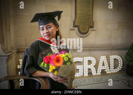 a pretty asian female graduate poses with flowers for photographs at her graduation day ceremony this formal event where graduands before change in 2hwcebn