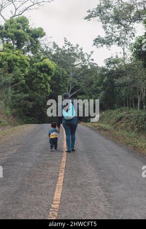 woman holding child by the hand on the road in a nature environment, walking on her back Stock Photo