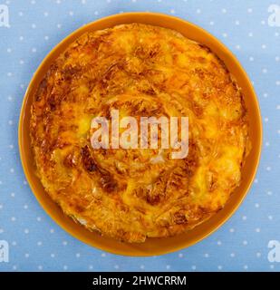 Top view of national festive Bulgarian cheese filo pie Banitsa served on clay plate on blue tablecloth Stock Photo