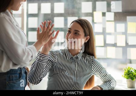 Two asian woman colleagues give each other high five, Successful business team working together concept. Stock Photo