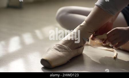 ballet dancer tie up her pointes. Ballet dancer tying ballet shoes before training. Stock Photo