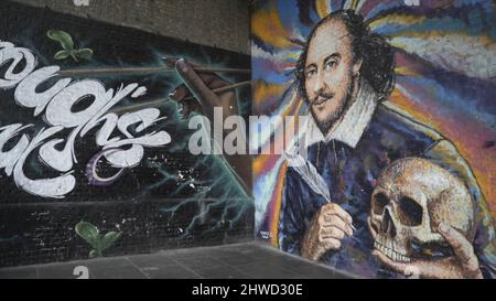 Close-up of the street musician playing guitar near the William Shakespeare's graffiti on the wall. Street performance in London Stock Photo