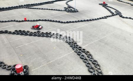 Aerial view of kart racers in protective uniform and helmet moving on the track with old black car tires in the city in sunny day. Karting Championshi Stock Photo