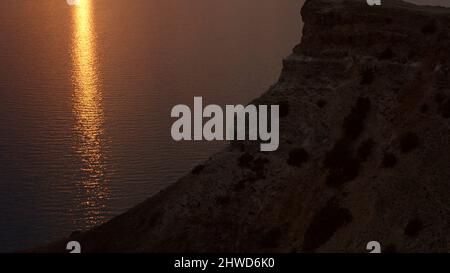 Sunset view at the seashore of cliffs and rocks. Shot. Top view of the sunset on the beach with rocks. Stock Photo