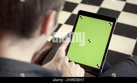 Close-up of man holding tablet and touching green screen. Stock fooatge. Young freelancer uses tablet to work or create projects. Tablet with green sc Stock Photo