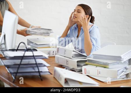 Nooo Too much paperwork. A young businesswoman looking frustrated as shes handed more paperwork. Stock Photo