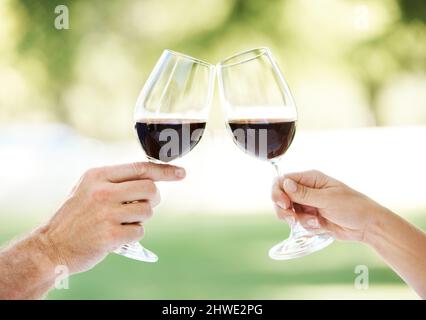 To us. Cropped view of a couples hands toasting with two glasses of wine. Stock Photo