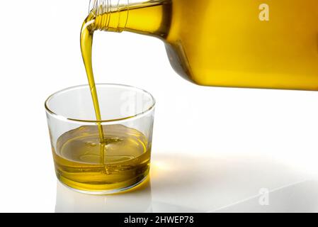 Extra virgin olive oil being poured from bottle into glass cup on white background Stock Photo