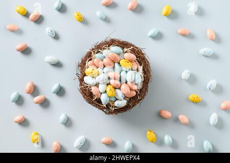 Easter colorful chocolate eggs in decorative nest isolated on blue background. View from above. Flat lay. Stock Photo