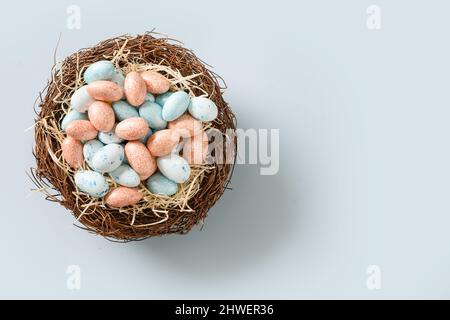 Easter colorful chocolate eggs in decorative nest isolated on blue background. View from above. Flat lay. Space for text. Stock Photo
