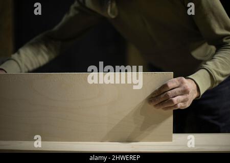 Carpenter holds board making furniture. Hand holds piece of wood. Work in carpentry workshop. Stock Photo