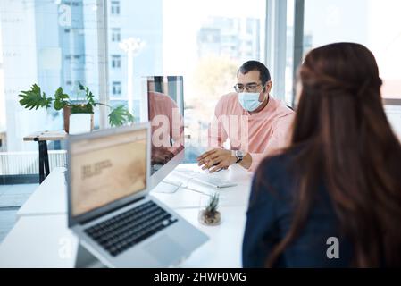 Staying shielded while achieving success. Shot of two businesspeople wearing face masks while working together in an office. Stock Photo