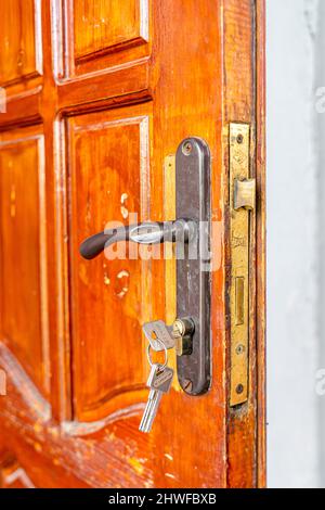 Keys in the lock and the door handle on the old open wooden door Stock Photo