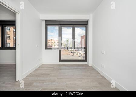 Empty living room with wood-like stoneware floors, large windows overlooking a square Stock Photo