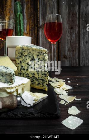 Brie cheese board combined with blue cheese and several cheese knives, Parmesan cheese shavings and wine glasses, a cactus in a white pot and a rustic Stock Photo