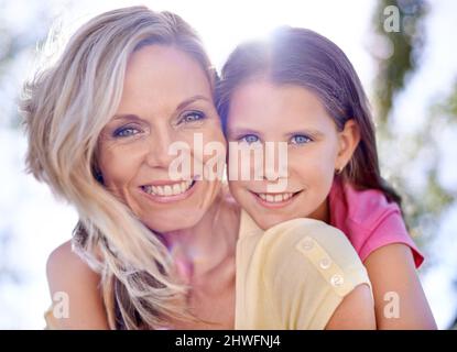 Sharing matching smiles. A smiling mother with her daughter on her back while outdoors. Stock Photo