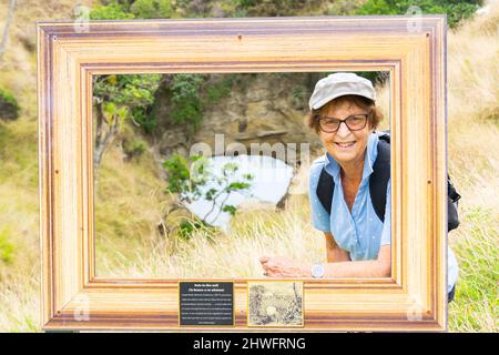 Tourist in frame, set up for travelers to pose in front of Hole In Wall attraction on walk to Cooks Cove on East Coast New Zealand. Stock Photo