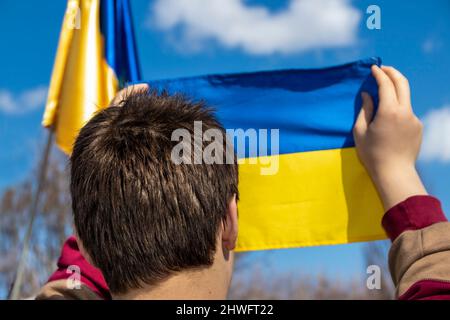 Head of young man holding up small Ukrainian flag at outdoor rally with another blurred flag in background- selective focus Stock Photo