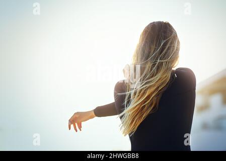 She stretches before every surf. Rearview shot of an unrecognizable young female surfer warming up on the beach. Stock Photo