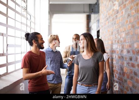 Catching up on the way to class. Shot of a diverse group of university friends talking in a hallway. Stock Photo