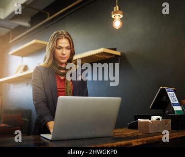 Working on some marketing strategies online. Cropped shot of a young business owner using a laptop in her shop. Stock Photo