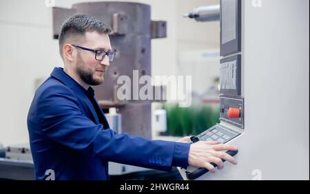 Young man worker operating CNC turning machine in modern factory industry. Stock Photo