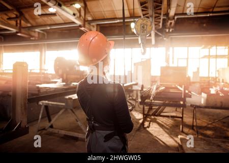 Woman engineer in hard hat operates industrial beam crane lift in factory. Stock Photo