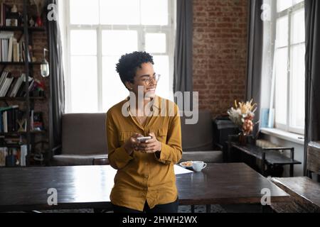 Happy dreamy Black freelancer woman using smartphone Stock Photo