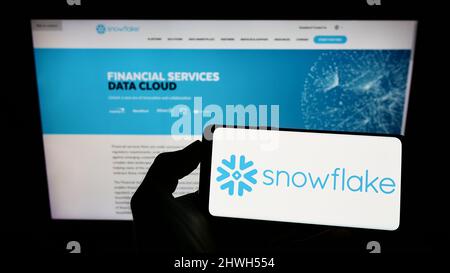 Person holding cellphone with logo of US software company Snowflake Inc. on screen in front of business webpage. Focus on phone display. Stock Photo