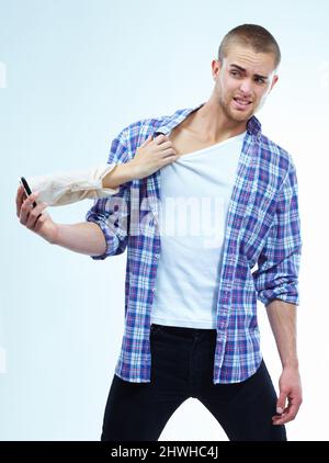 The pull of modern technology. A handsome young man having his shirt pulled by the hand coming out from the cellphone. Stock Photo
