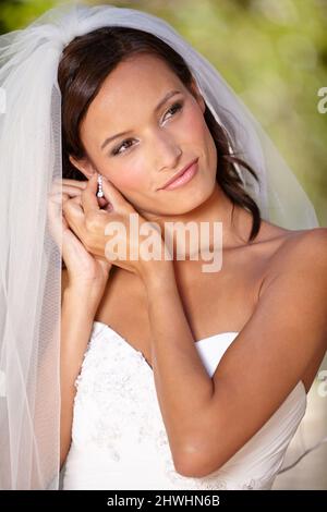 Last minute adjustments. Beautiful bride adjusting her earrings on her wedding day. Stock Photo