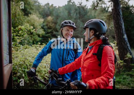 Happy senior couple bikers talking by map outdoors in nature in autumn day. Stock Photo