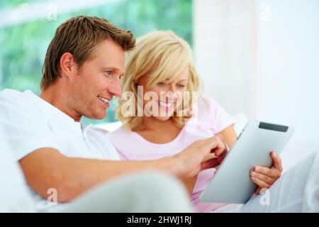 Happy couple using tablet pc. Happy couple sitting on a sofa using tablet pc. Stock Photo