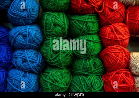 Many wool yarns in bright colours stacked on the shelf in store, rows of navy blue, sky blue, green and red coloured wool balls for sale. Knitting Stock Photo