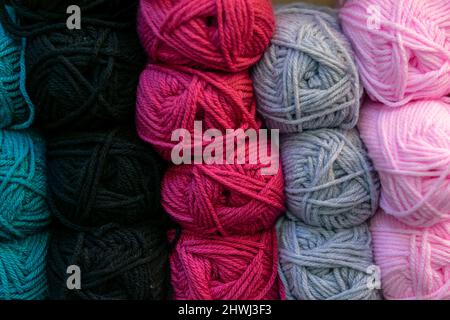 Many wool yarns in bright colours stacked on the shelf in store, rows of blue, black, magenta, grey and pink coloured wool balls for sale. Knitting Stock Photo