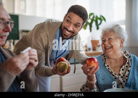 Caregiver bringing healthy snack to senior woman and man in nursing home care center. Stock Photo