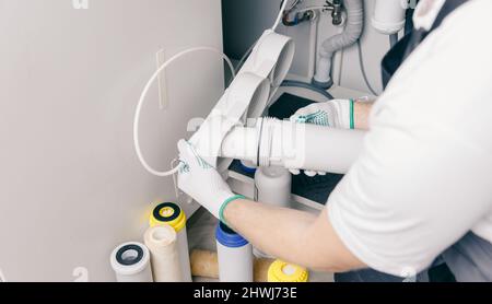 Plumber working install new cartridge for cold water filter in white kitchen. Stock Photo