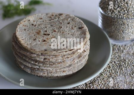 Soft flat bread made of pearl millet flour. Shot on white background along with a heap of pearl millet inside a small glass bowl. Commonly called bajr Stock Photo