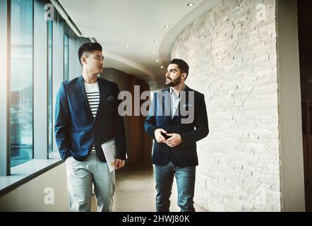 Success is all about the nows and tomorrows. Shot of two young businessmen walking and talking in a modern office. Stock Photo