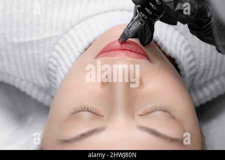 Macro photo of process of applying permanent makeup tattoo of red on lips woman. Stock Photo