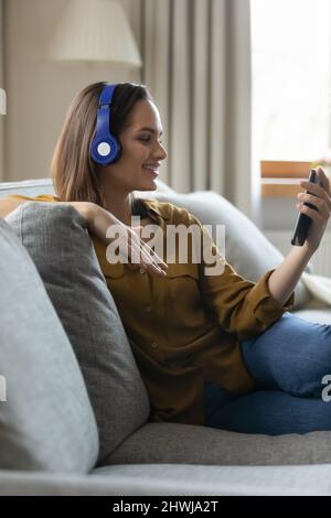 Smiling woman wear headphones holds smart phone watch video clip Stock Photo