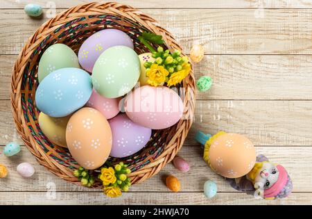 Colorful easter eggs and yellow flowers in a basket on a wooden table.  Overhead view with copyspace Stock Photo