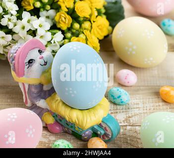 Easter rabbit figurine with colorful eggs and flowers in background on a wooden table Stock Photo