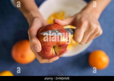 Close up on hands of unknown caucasian woman peeling red apple over the bowl on the table at home - healthy eating concept organic food homemade veget Stock Photo