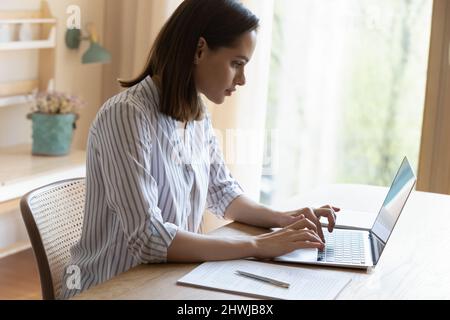 Serious businesswoman sit at table types texting on laptop keyboard Stock Photo