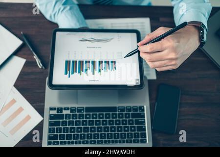 Business hand hold stylus pen touch screen digital tablet with business diagram on the table workspace. Stock Photo