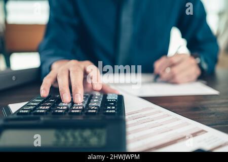 Financial businessman working on desk office using a calculator to calculate calculating corporate income tax data And analyzing charts of financial. Stock Photo