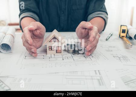 Architect engineer hands protact house and money coin on bueprint. Cost House planning design and construction concept. Stock Photo